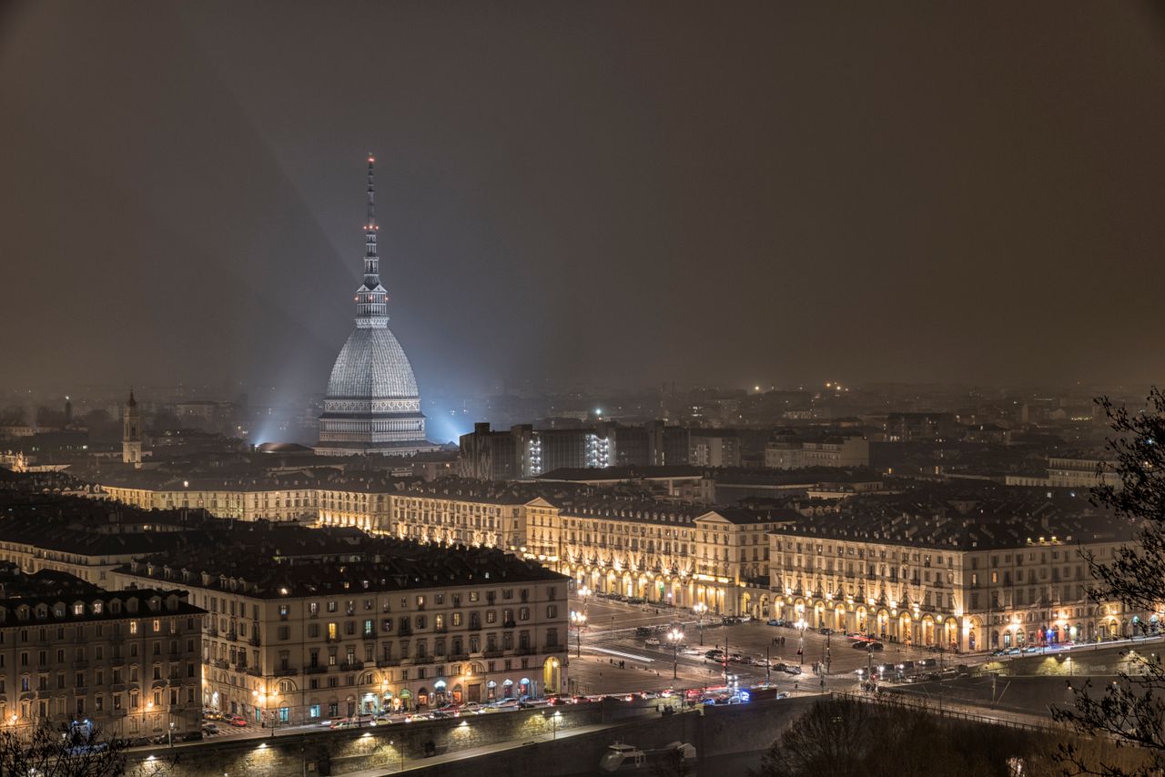 Stunning night view of Torino cityscape featuring Mole Antonelliana illuminated amidst historical buildings.
